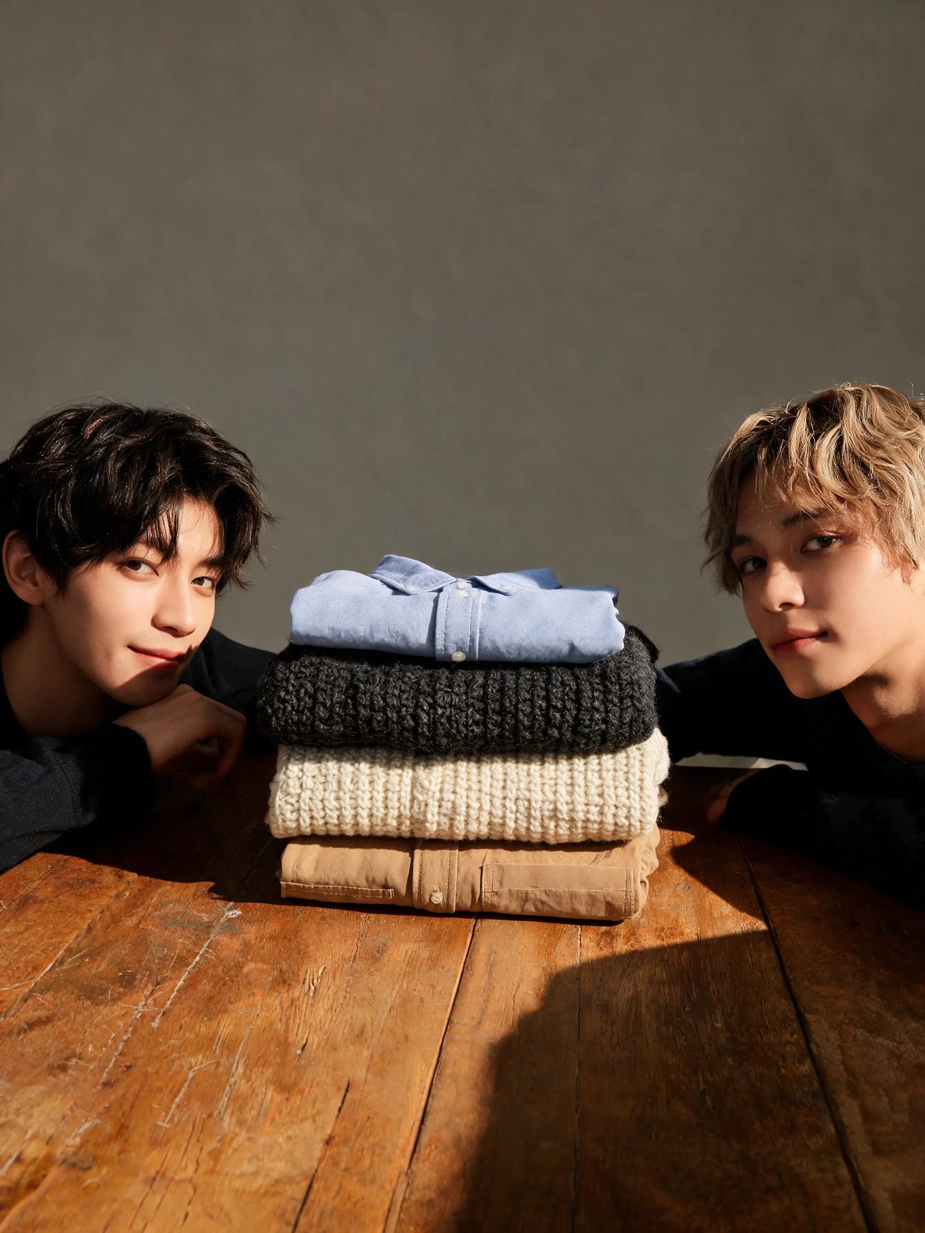 Folded knitwear and shirts stacked on a worn oak table